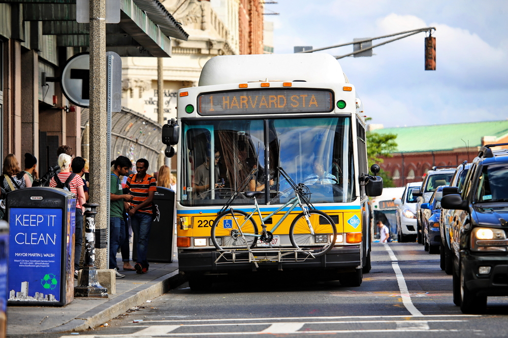 A bus with a bike rack alongside cars on road in Boston