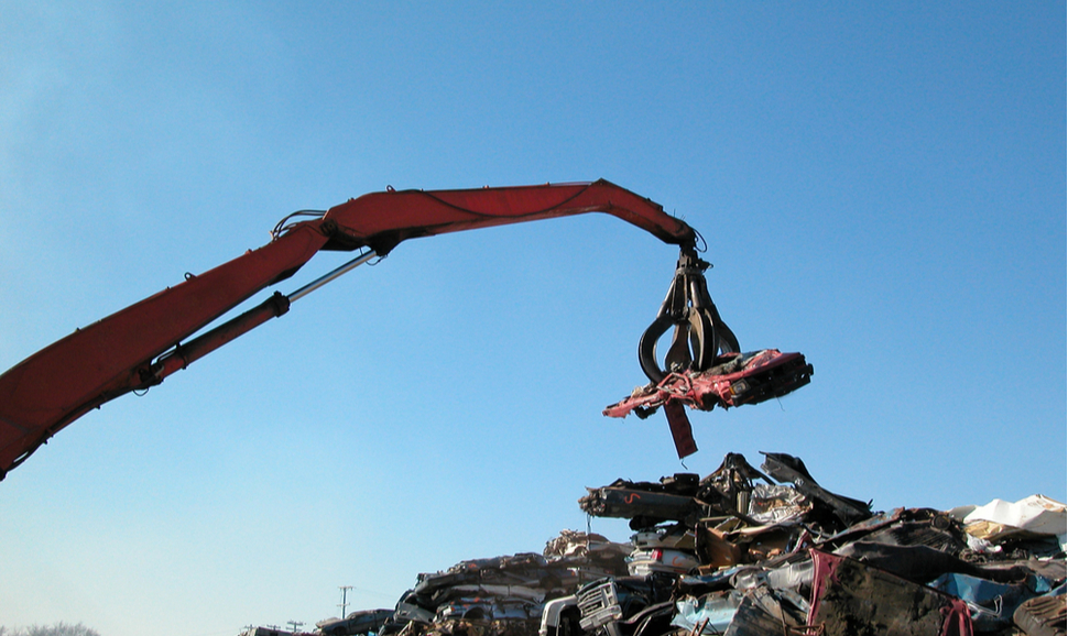 Claw crane picking up an old car to be recycled in a scrap yard