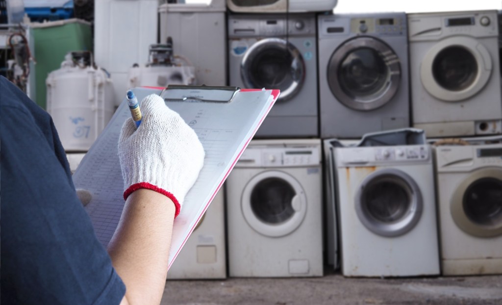 Worker with a clipboard in front of discarded washing machines.