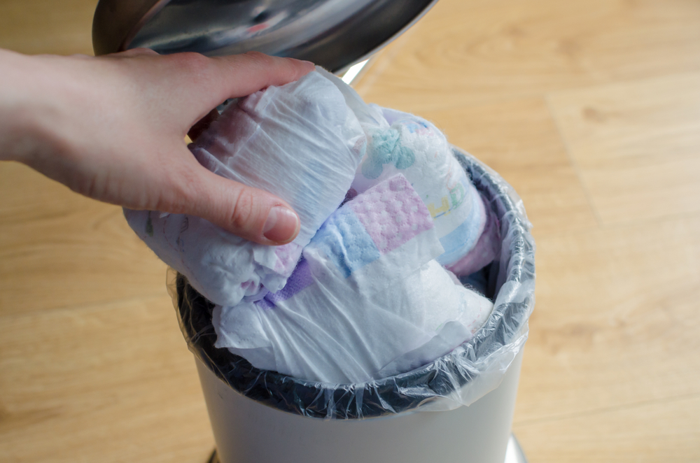 Person putting diaper in trash bin filled with more diapers