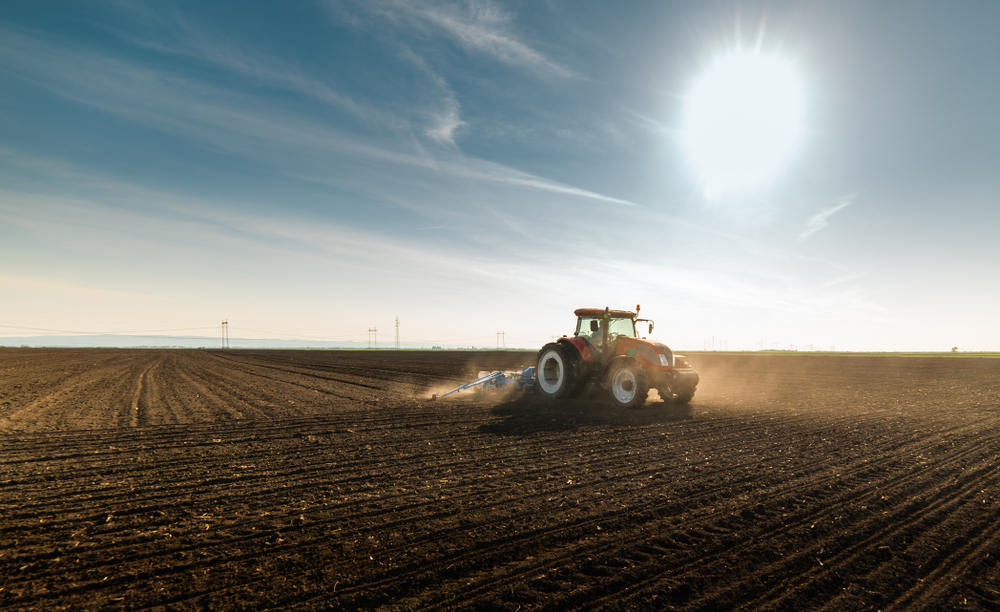 Farmer with tractor seeding crops at agricultural field