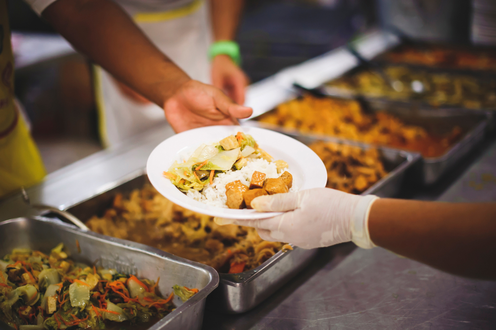 One person handing another person food on a white plate