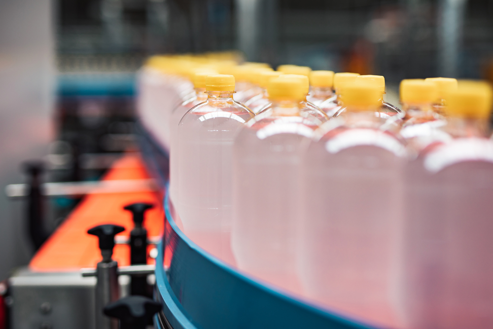 Clear plastic bottles with yellow tops on conveyer belt to be processed and filled with contents.