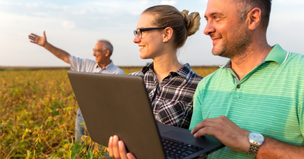 Group of farmers with laptop standing in a field examining soybean crop