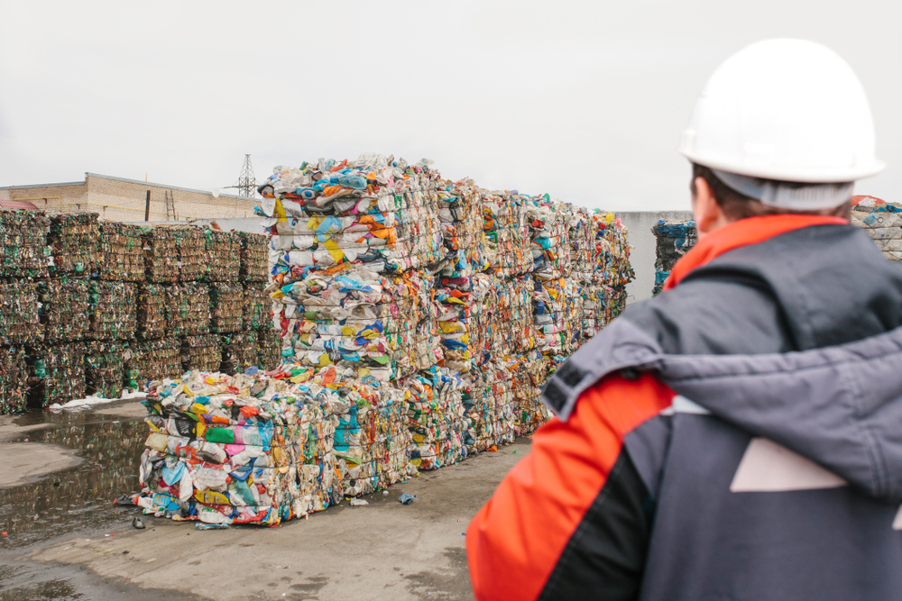 Worker looking at bundles of recyclable materials at waste processing plant.