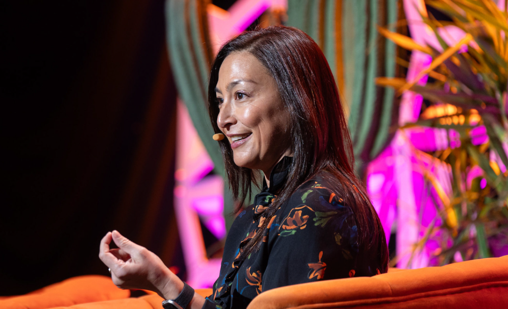 Portrait of woman with black hair speaking on stage.