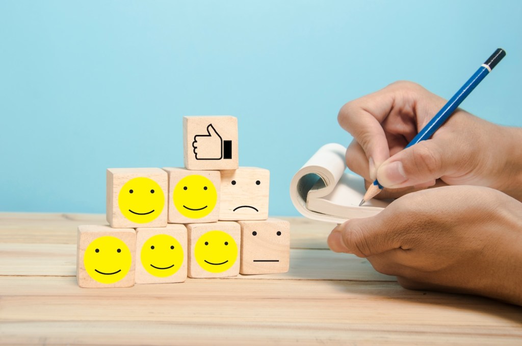 Hand noting feedback on a notepad, with smiley phases and neutral phases.