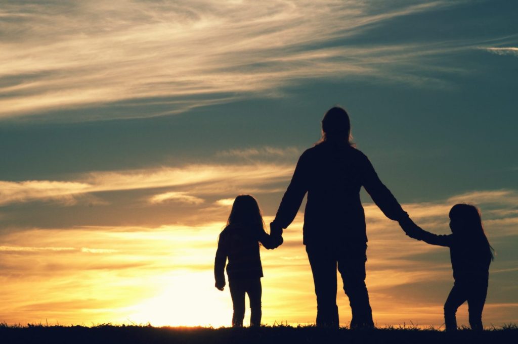 Adult holding hands with two children in front of a sunset.