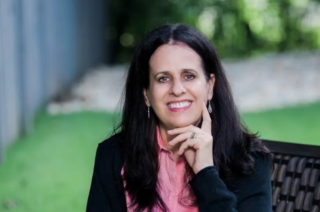Rochelle Routman (Portrait of women with black suit, pink shirt and long black hair.)