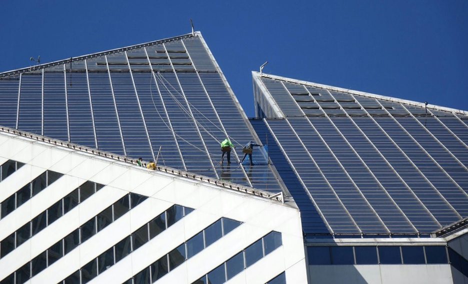 Solar technicians clean panels on a corporate building's roof.