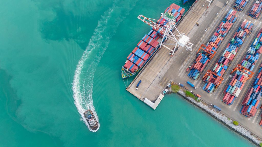 Crane loading box container to cargo ship at commercial dock port.