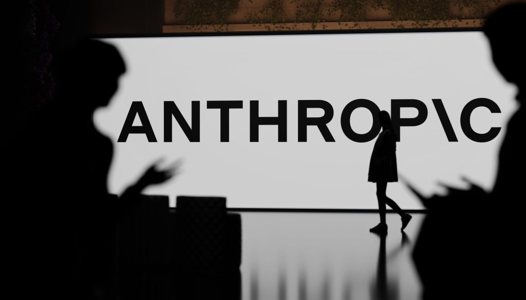 Silhouette of a person on stage in front of a large display reading 