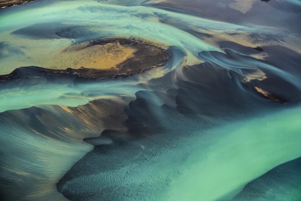 Turquoise river flows through dark brown glacial river delta.