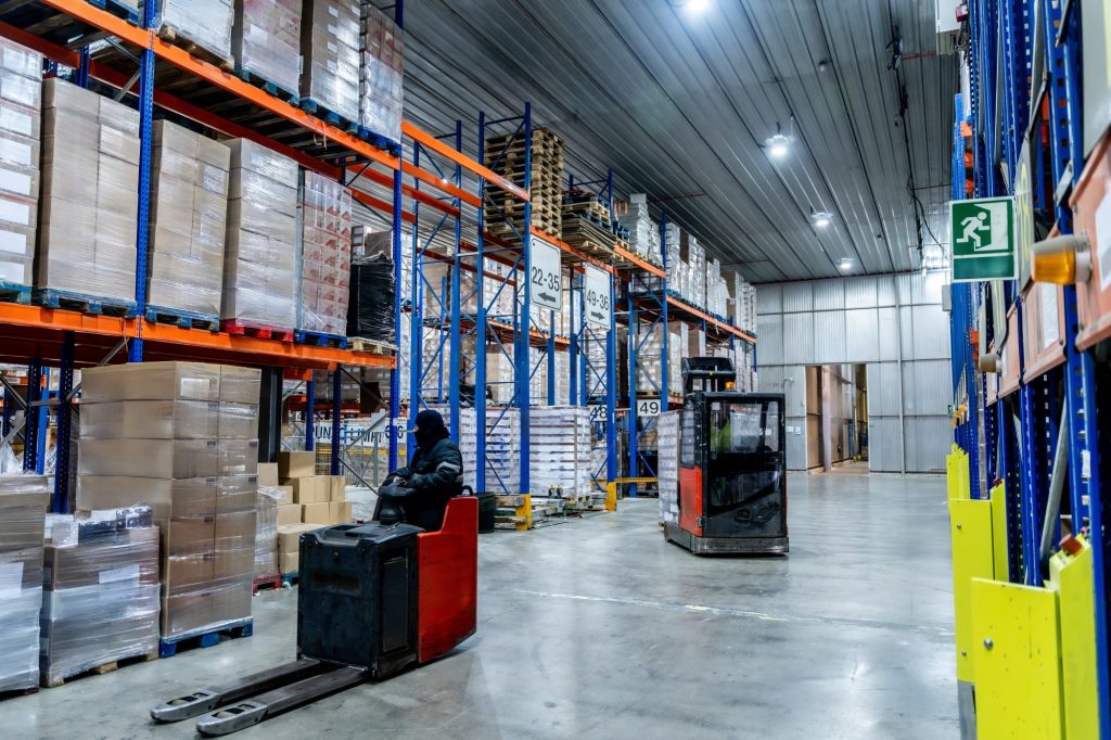 Workers managing inventory with forklifts, navigating between tall shelving units stacked with goods on pallets in a vast, modern cold storage facility